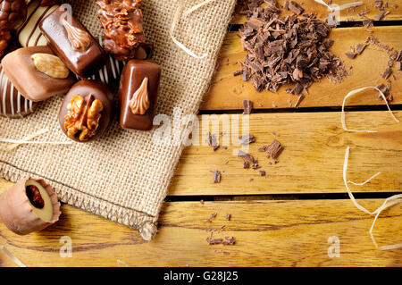 Group of bonbons stacked on a wood table close up. Black and white chocolate with nuts and straw decoration . Top view. Stock Photo