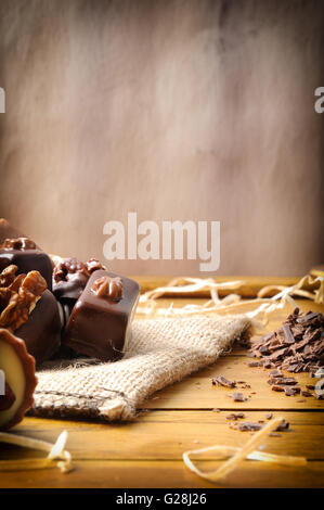 Group of bonbons stacked on a wood table close up. Black and white chocolate with nuts and straw decoration . Front view. Stock Photo