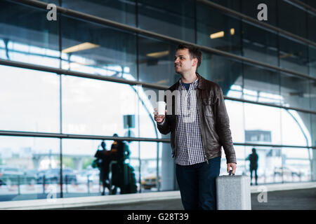 Portrait of a young man walking near the airport with suitcase and coffee Stock Photo