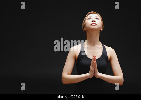 Attractive young Japanese woman wearing black pants and tank top practicing yoga on black background Stock Photo