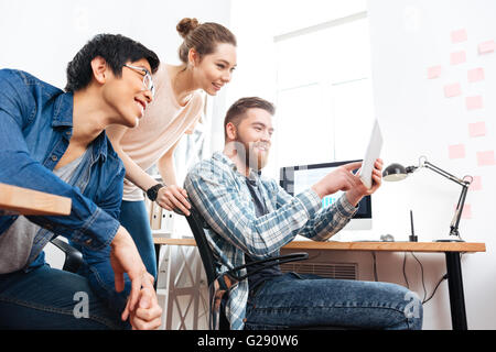 Three smiling young businesspeople working with tablet in office Stock Photo