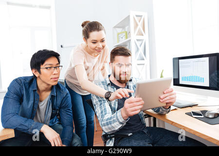 Three focused young businesspeople working in office together and using tablet Stock Photo