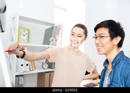 Two cheerful young businesspeople writing on flipchart in office Stock Photo