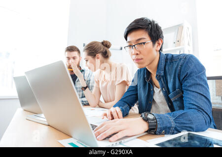 Three focused young businesspeople working in office with laptops Stock Photo
