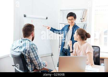 Smilling asian young man making presentation to his colleagues and using flipchart Stock Photo