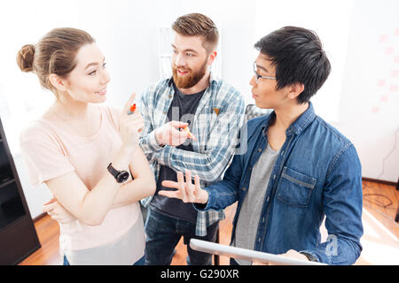 Cheerful young businesspeople standing and discussing bisness plan using tablet in office