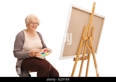 Mature woman mixing colors on a color palette and posing next to a canvas isolated on white background Stock Photo