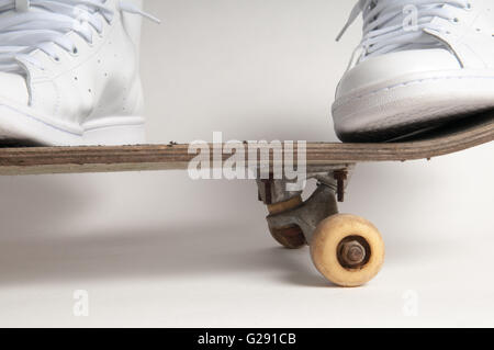 Man in clean white trainers doing tricks on an old skateboard Stock Photo