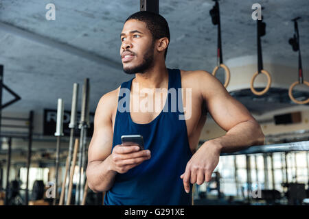 Pensive sports man holding smartphone while resting in the gym Stock Photo