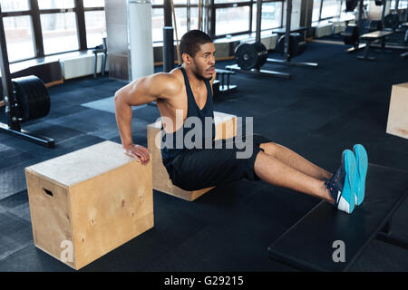 Strong fitness man pumps biceps using training apparatus in the gym Stock Photo