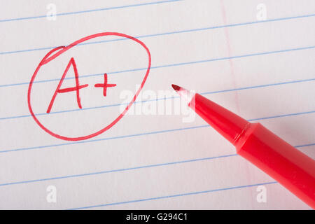 A plus (A+) grade written in red pen on notebook paper with the pen sitting there. Stock Photo