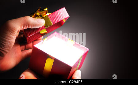 hands opening a red gift box with gold ribbon in shadow. Horizontal composition. Top view. Stock Photo