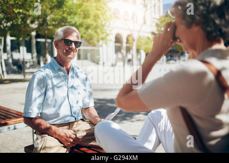 Handsome senior man being photographed by his wife. Senior tourist talking photos with camera outdoors in the city. Stock Photo