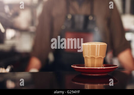 Close up shot of coffee cup with saucer on cafe counter with barista standing in background. Stock Photo