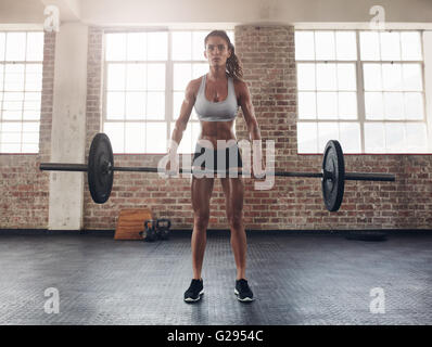 Full length image of tough young woman exercising with barbell. Determined female athlete lifting heavy weights.