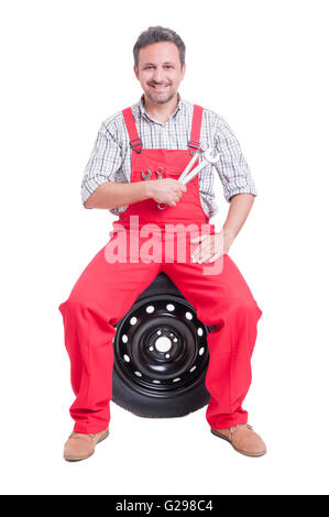 Friendly auto mechanic holding keys sitting on car wheel Stock Photo