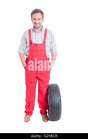 Friendly and trustworthy mechanic standing with hands in pockets newa a wheel tire isolated on white Stock Photo