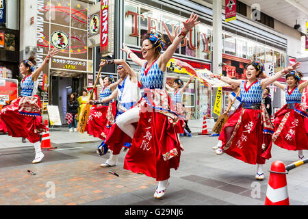 Japan, Kumamoto. Hinokuni Yosakoi dance festival. Team of Japanese young woman dancers, arms outstretched, dancing in formation in shopping arcade.