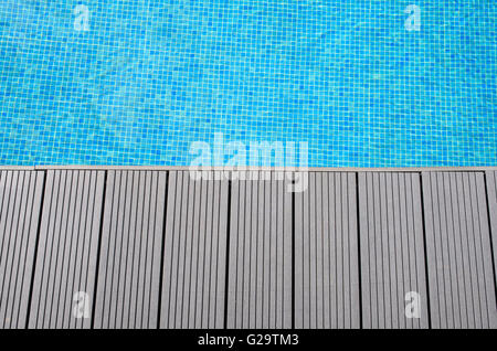 Decking at the edge of blue mosaic tiled swimming pool Stock Photo