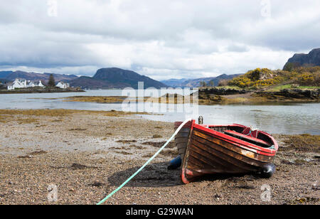 A weathered red boat on the beach in the village of Plockton, Ross Shire in Scotland UK Stock Photo