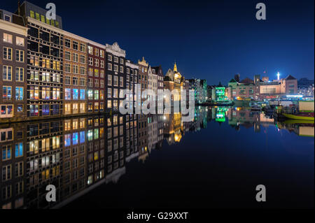 Beautiful traditional old houses at night in Amsterdam, Netherlands. Cityscape with reflected city buildings in water with blue Stock Photo