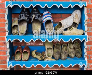 Several old wooden shoes on a blue painted wooden rack against a brick wall. Stock Photo