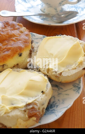 Buttered fruit scones and afternoon tea on china plates Stock Photo
