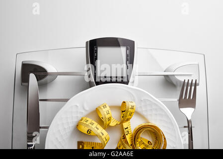 Cutlery with yellow tape measure on a scale plate on a white table. Concept of healthy eating at the table. Horizontal Stock Photo