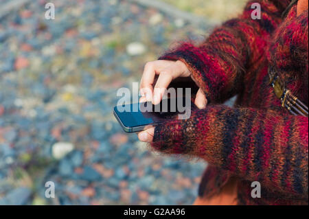 A young woman is using her smartphone outside with gravel and rubble on the ground Stock Photo