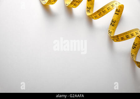 Yellow tape measure in meters and inches in a spiral on white table. Top view. Horizontal composition. Stock Photo