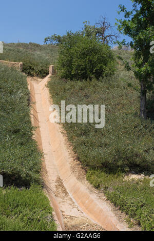 Dry water culvert runs downhill through a planted hillside in drought California. Stock Photo