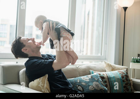 Father sitting on sofa and playing with baby daughter (2-5 months) Stock Photo