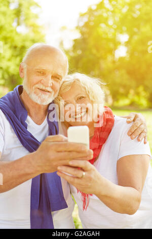 Happy senior couple taking a selfie with smartphone in a fall garden Stock Photo