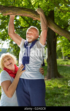 Old man doing pull-ups on a tree in a summer park Stock Photo