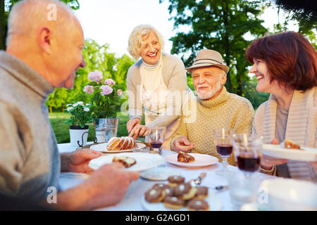 Happy seniors at birthday party sitting with cake in the garden Stock Photo
