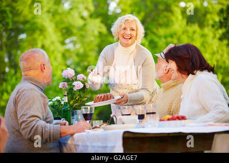Woman serving ring cake at birthday party with senior people in a garden Stock Photo