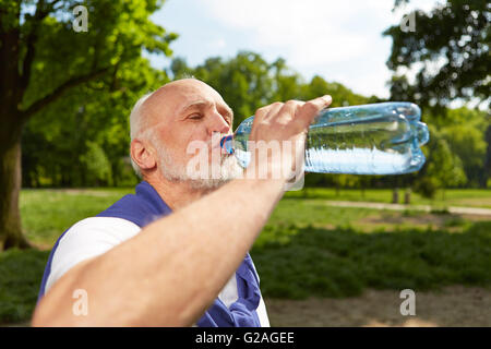 Thirsty senior man drinking a bottle of fresh water after doing sports Stock Photo