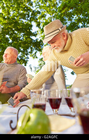 Happy senior friends playing cards together in a garden in fall Stock Photo