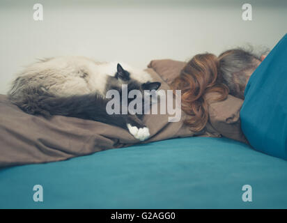 A young woman is sleeping in a bed with a cat next to her