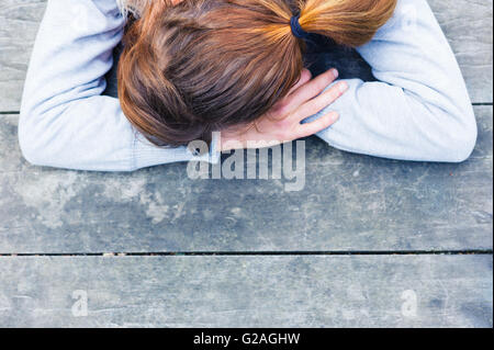 A sad young woman with her head resting on her hands at a table in the park Stock Photo