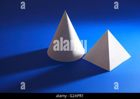 Geometry concept. White paper cone near pyramid on blue background Stock Photo