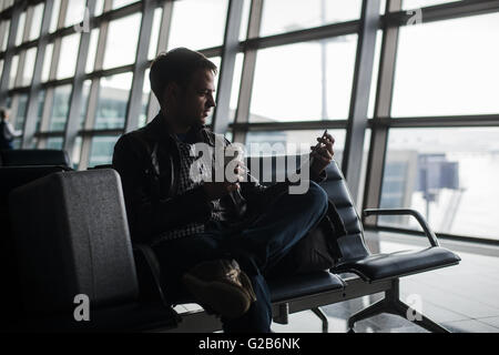 man waiting at airport lounge texting with his smart phone Stock Photo