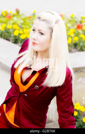 the bright beautiful blonde in a red suit at a flower bed Stock Photo