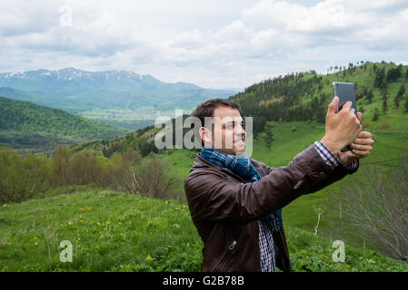 Happy young man smiling and making selfies holding tablet PC in the mountains Stock Photo