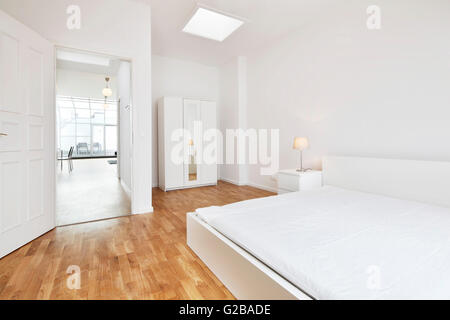 Conversion of Dach or Loft Space in Reichenberger Strasse, Kreuzberg. Modern white bedroom with minimal furniture and decoration. White walls and wood floor. View of rest of loft through open bedroom door Stock Photo