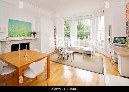 Pembridge Square, Notting Hill. Open plan contemporary living and dining area. White furniture with a wood floors. Painting hanging anove fireplace. Large windows. Stock Photo