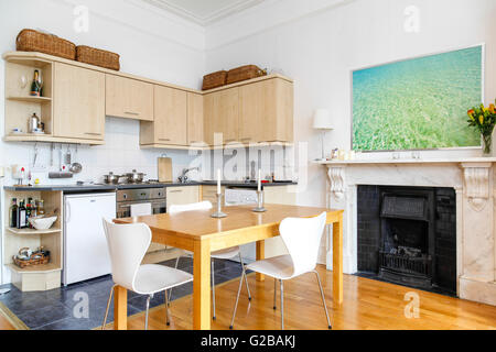 Pembridge Square, Notting Hill. View of a contemporary kitchen and dining area. Wood table and white chairs on top of wood floor. Picture hanging above fireplace. Stock Photo