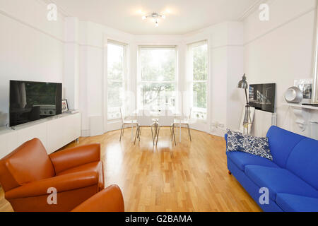 Pembridge Square, Notting Hill. Open plan living and dining room with bay windows and colourful sofa and chairs. Flat screen tv on side table. Wood floors with modern floor lamp. Stock Photo