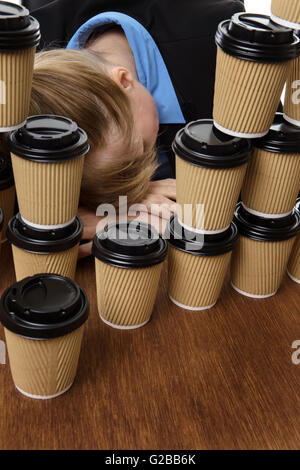 business woman has fallen asleep on the desk behind lots of takeaway drink cups. Stock Photo