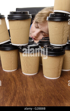 business woman has fallen asleep on the desk behind lots of takeaway cups. Stock Photo